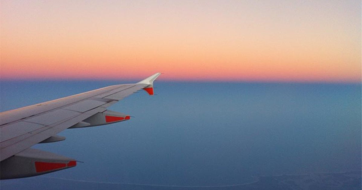 Flygplansvinge mot en horisont i solnedgång.