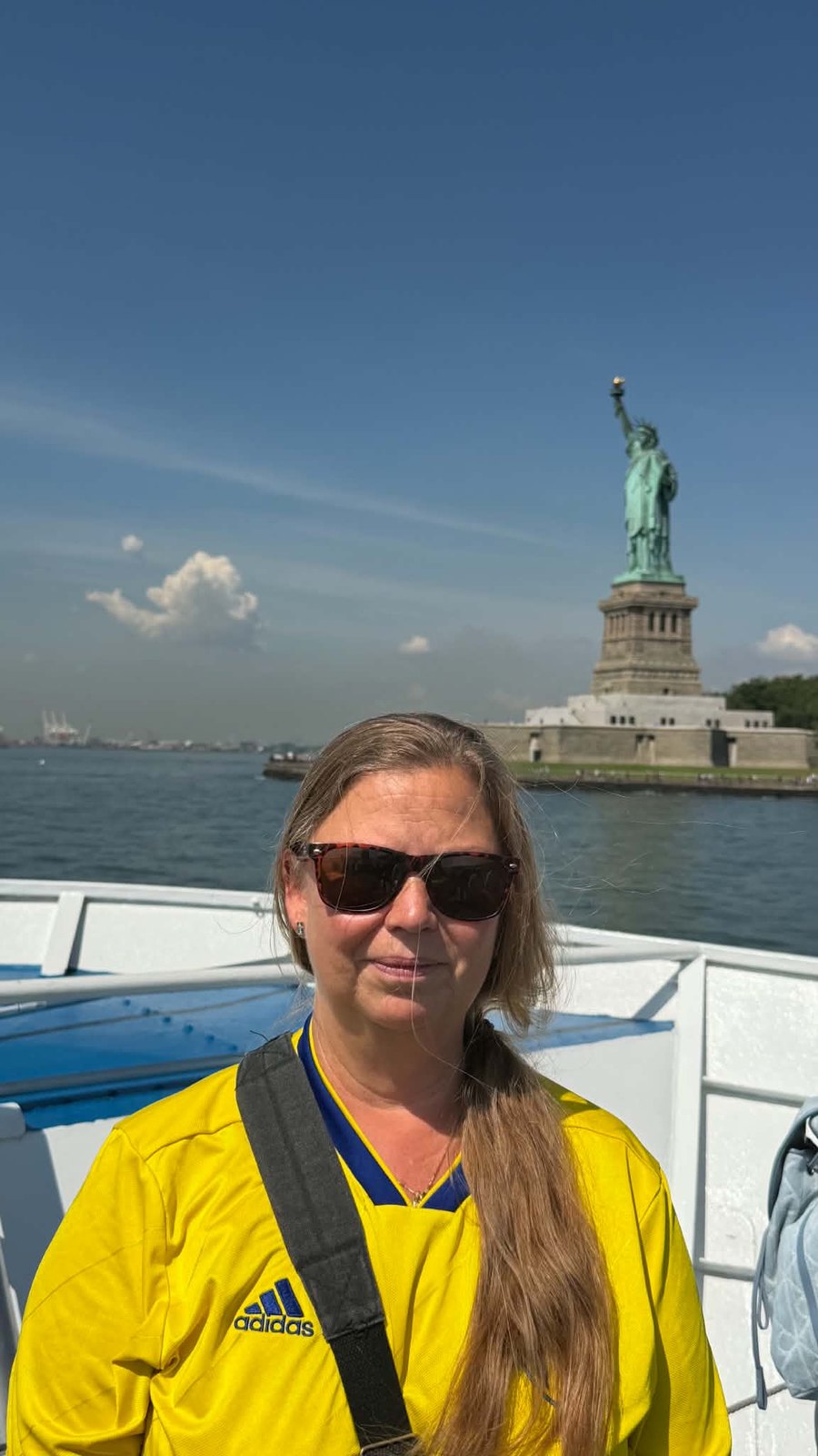 Susanne Petersson i gul landslagströja på en båt med Frihetsgudinnan i bakgrunden.